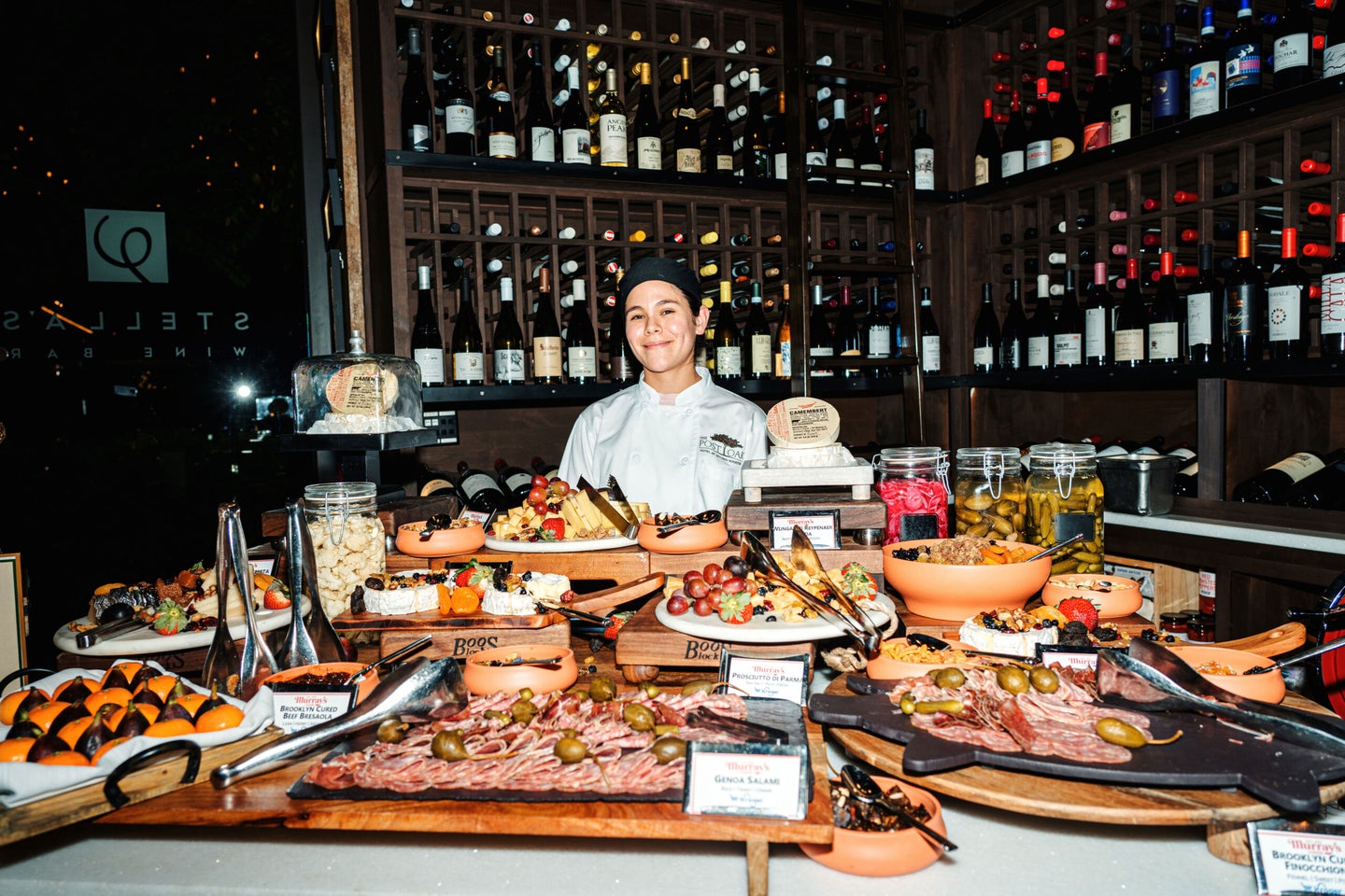 A chef stands behind an extravagant cheese and charcuterie grazing table in Stella's Wine Bar.